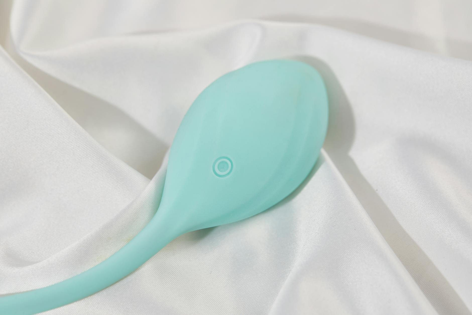 A teal vibrator resting on white silk fabric, symbolizing intimacy and pleasure