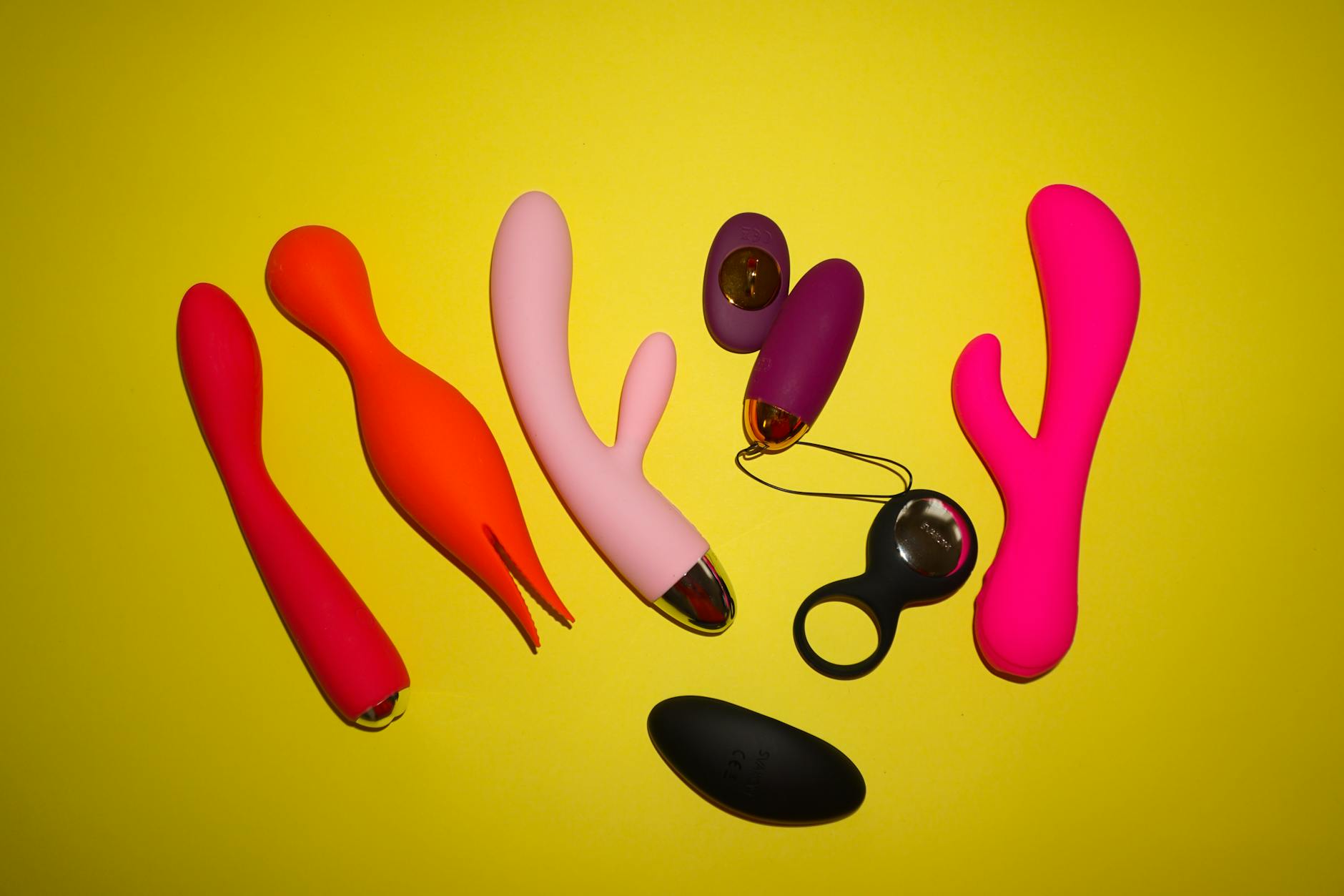 Colorful clitoral vibrators arranged on a bright yellow background, showcasing various shapes and textures